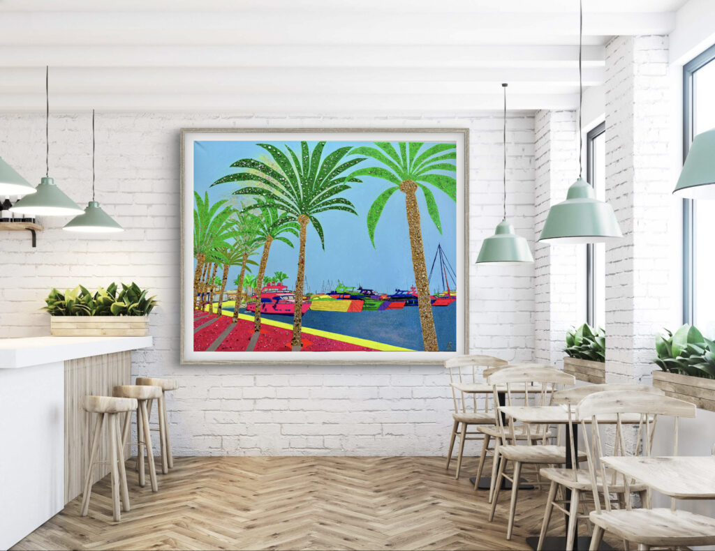 A bright, colorful artwork featuring palm trees and boats is displayed on a white brick wall in a modern cafe. The interior has wooden furniture, potted plants, and pendant lights, creating a vibrant and inviting atmosphere.