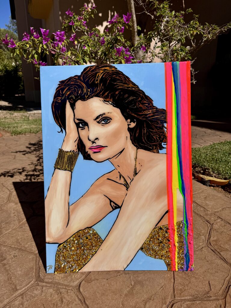 A colorful portrait of a woman with styled hair, wearing a glittery outfit. She is resting her head on her hand, set against a light blue background. Vivid rainbow stripes accent one side of the artwork, which is displayed outdoors with greenery and flowers in the background.