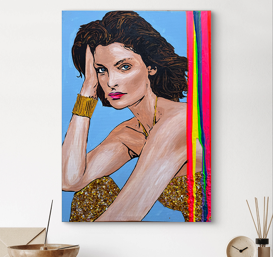 A colorful painting of a woman with wavy brown hair, wearing a glittery gold outfit, posing thoughtfully with one hand on her forehead. The background features a light blue color with vibrant vertical streaks of red and pink. The artwork is displayed on a wall above a decorative bowl and a round object on a table.